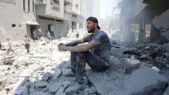 Mwanamume wa Kipalestina akiwa ameketi kwenye vifusi vya majengo yaliyoharibiwa kufuatia mashambulizi ya Israel dhidi ya kambi ya wakimbizi ya Al-Shati mjini Gaza.