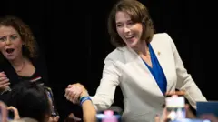 Crawford, con chaqueta blanca, le da la mano a una de sus seguidoras y sonríe 