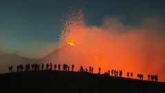 Люди стоят на горе и смотрят извержение вулкана.