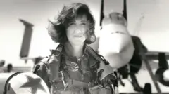 Donanma taktik uçaklarını kullanan ilk kadınlardan biri olan Teğmen Tammie Jo Shults, bir F/A-18'in önünde poz veriyor. Pilot tulumu giymiş ve kaskını sağ elinde tutuyor.