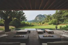 Terraza contemporánea cubierta con camas lounge y fogones, abierta a un paisaje verde con montañas al fondo.