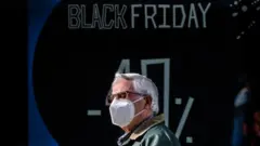 Homem usando máscara passa diante de vitrine que anuncia desconto da Black Friday