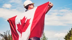 A man holding Canada flag for im back wit helmet for im head. 
