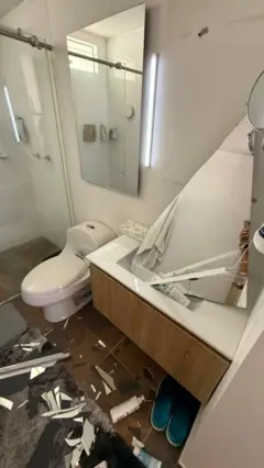 O banheiro do apartamento de Molina, com um espelho quebrado e vários objetos e destroços espalhados pelo chão.