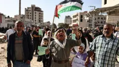 Жители лагеря беженцев Нур Шамс, расположенного недалеко от Тулкарма на оккупированном Израилем Западном берегу, протестуют под палестинским флагом у входа в лагерь, требуя права вернуться в свои дома. На заднем плане - полуразрушенные дома