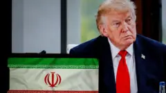 في هذه الصورة التوضيحية، يظهر الرئيس الأمريكي دونالد ترامب خلف العلم الإيراني، بينما تُعرض جميعها على الشاشات، في مدينة ليون الفرنسية بتاريخ 2 يوليو/تموز 2026