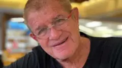 На фотографии, сделанной при жизни, Годдард, с короткими светлыми волосами, в очках с красной оправой и в черной футболке, улыбается в камеру.