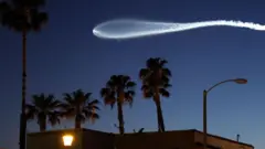Trilho branco brilhante de um foguete Falcon 9 transportando 25 satélites de internet da Starlink contra o céu escuro, acima de uma construção e palmeiras, em Pasadena, no Estado americano da Califórnia, no dia 6 de abril de 2026