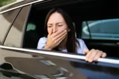 গাড়ির জানালার কাছে মুখে হাত রেখে বমির ভাব করছেন একজন নারী