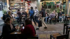 مردم در یک کافه روباز در مرکز شهر تهران، ایران، در ۱۱ آوریل ۲۰۲۶ (۲۲ فروردین ۱۴۰۵) گرد هم آمده‌اند، همزمان با برگزاری مذاکرات مستقیم ایران و ایالات متحده در اسلام‌آباد پاکستان