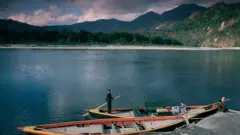 Imagem de um lago e uma pessoa ao lado de dois barcos