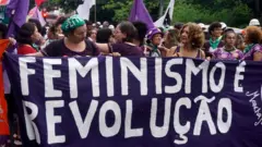 Mulheres durante manifestação segurando uma faixa "Feminismo é revolução"