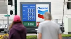 ガソリンスタンドに表示されている価格を、歩道から男女が見ている