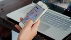 Seseorang memegang ponsel di depan laptop