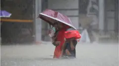 সিলেটে বৃষ্টি ও বন্যার মধ্যে সন্তানদের নিয়ে নিরাপদ আশ্রয়ে যাচ্ছেন একজন নারী