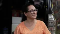 Renata, de camisa laranja, aparece de perfil sorrindo