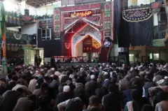 په یوه تکیه خانه کې ګڼ خلک راټول دي او یو امام وینا ورته کوي.