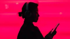 Woman in silhouette listening to music on smarphone in front of a bright pink background