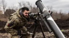 Український солдат дивиться в приціл міномету