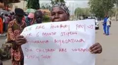 Iya agbalagba kan lara awon olufẹhonuhan naa gbe akọle to n kede pe Gomina Aiyedatiwa jẹ wọn lowo oṣu mẹfa dani