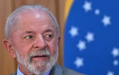 Presidente Lula olhando para a direita com a bandeira do Brasil ao fundo