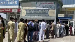 Jama'a na layi a kofar bankin AZIZI domin karbar kudin ajiyarsu yayin da ake fama da matsalar karancin kudi a Kabul