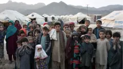 Children pose for photographs in front of their tents at a camp for internally displaced families in Panjwai district of Kandahar province