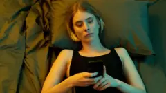 Chica con un teléfono en la mano en la cama.