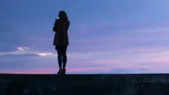 امرأة تصور الغروب بهاتف محمول