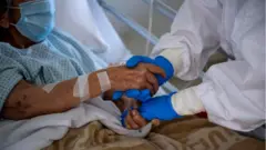 ROME, ITALY - APRIL 14: (EDITORIAL USE ONLY) A medical worker greets a patient suffering from COVID-19 in an intensive care unit (ICU) in the Covid department of Rome's San Filippo Neri Hospital on April 14, 2020, in Rome, Italy. There have been well over 160,000 reported coronavirus (COVID-19) cases in Italy and more than 20,000 related deaths, but the officials are confident the peak of new cases has passed.