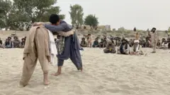 دو کودک افغان کشتی می گیرند و دیگران تماشا می‌کنند