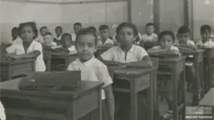 Crianças em escola no Rio, sentadas em suas cadeiras, olham para câmera 