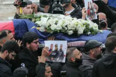 İsrail saldırılarında öldürülen üç gazetecinin cenazesinde omuzlarda taşının çiçeklerle bezeli bir tabut ve gazetecilerin fotoğrafını tutan bir el görünüyor