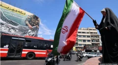 Obìnrin tó wọ aṣọ dúdú, tó mú àsíá Iran dání, àwon ọkọ̀ àti ọ̀kadàwà lẹ́yìn rẹ̀