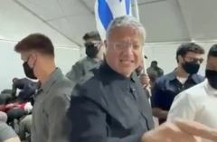 Bir adam elinde İsrail bayrağı birilerini taciz eder gibi görünüyor, yanıda güvenlik görevlileri var.