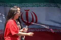 Hai người phụ nữ đi ngang qua quốc kỳ Iran tại quảng trường Vanak ở Tehran vào ngày 10/6/2026