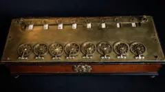 Máquina construída em madeira e bronze, com rodas numeradas que permitem os cálculos
