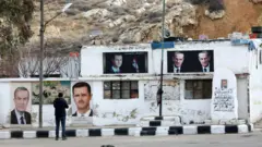 رجل يلتقط صورة لمبنى يحمل صور الرئيس السوري المخلوع بشار الأسد ووالده الراحل والرئيس السابق حافظ الأسد، داخل قاعدة الحرس الجمهوري السوري المهجورة على جبل قاسيون المطل على دمشق في 4 يناير 2025. 