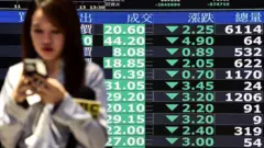 A woman walks past screens displaying average stock prices at the Taiwan Stock Exchange in Taipei on April 7, 2025