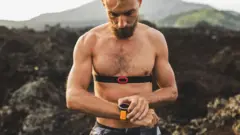 一名男子佩戴智能手錶和心率監測裝置，在山路上運動休息時，低頭看手錶