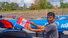 Uma pessoa em frente a uma lancha segurando uma bandeira do Peru nas mãos, na ilha Santa Rosa