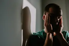 Un hombre sostiene su cabeza con sus dos manos. Su sombra se refleja en una pared.