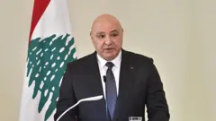 Президент Ливана Жозеф Аун на пресс-конференции, за ним флаг Ливана.