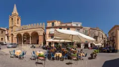 Praça com campanário e restaurante ao ar livre na Itália