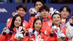 赤いそろいのウェアを着たチームのメンバーらが、首にかけたメダルを右手で持ち上げている。左手には大会マスコットのぬいぐるみを持っている。全員が笑顔を見せている