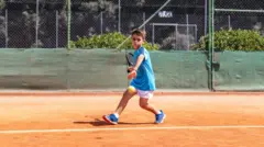 Menino jogando tênis em uma quadra de terra