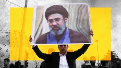 A treated image shows a man in a dark suit and white shirt holding up a banner of new Iranian supreme leader Mojtaba Khamenei. A yellow rectangle has been interposed behind the man and poster, and other figures mill about in the background