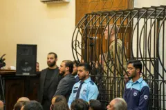 Ateb Najib está dentro de uma jaula, usando um uniforme listrado, enquanto é sentenciado em um tribunal em Damasco, Síria