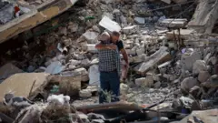 صورة تظهر رجلين يعانقان بعضهما وسط ركام مبنى مدمّر في لبنان