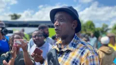 Umuntu w'umugabo wambaye ingofero, imbere ye hari za mikoro (micros) 
